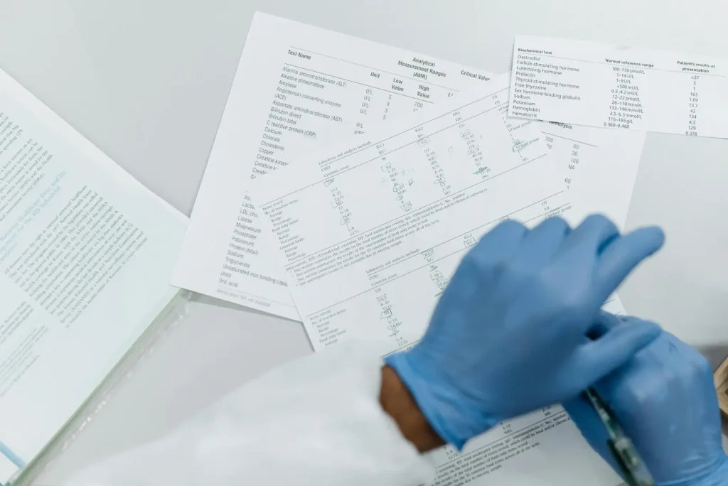 Normal lab test results next to a gloved hand reviewing bloodwork, representing the mind-body connection when labs look fine but symptoms persist